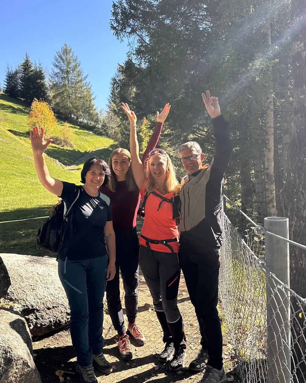 Mitglieder des TopFit Clubs jubeln mit erhobenen Armen bei der Wanderung im Sonnenlicht